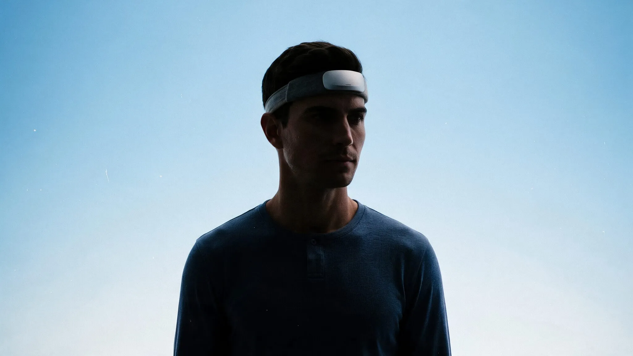 Homem com faixa de EEG na testa, em contraluz contra um céu azul