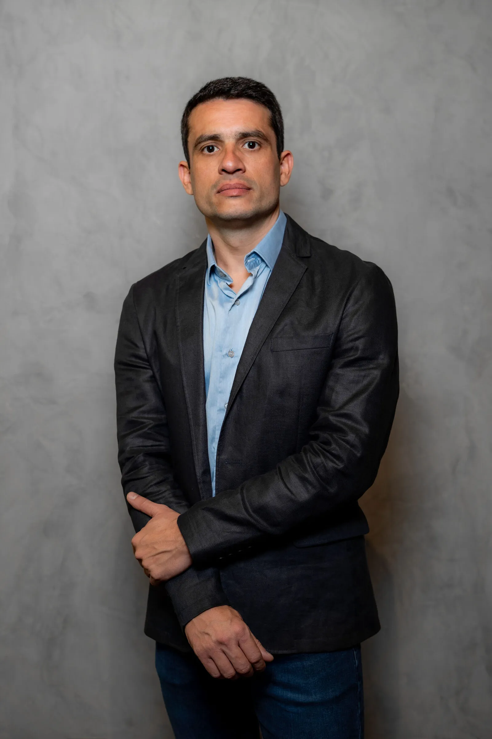 Dr. Thiago Faria Lacerda, de blazer escuro e camisa azul, contra uma parede de cimento