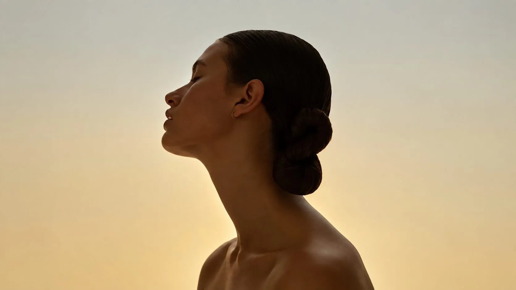 Mulher de perfil, olhos fechados, contra um céu dourado ao entardecer